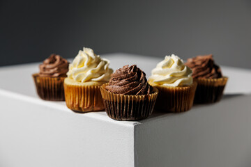 Five cupcakes with chocolate and vanilla frosting arranged neatly along the corner of a white pedestal, set against a dark gradient background with ample copy space
