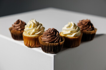 Five cupcakes with chocolate and vanilla frosting arranged neatly along the corner of a white pedestal, set against a dark gradient background with ample copy space