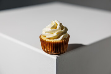 Single vanilla cupcake with smooth, swirled frosting placed at the edge of a white surface against a dark gradient background, with copy space