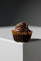 Decadent chocolate cupcake topped with dark swirled frosting, placed at the corner of a white surface against a dark gradient background with copy space