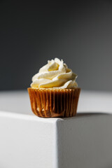 Single vanilla cupcake with smooth, swirled frosting placed at the edge of a white surface against a dark gradient background, with copy space