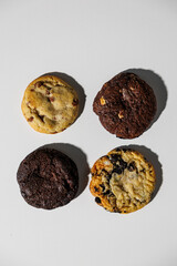 Overhead view of four different cookies—chocolate chip, double chocolate, chocolate chunk, and cookies and cream—arranged neatly on a white surface with copy space