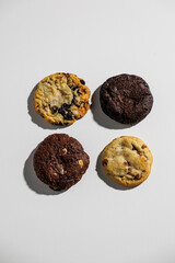 Overhead view of four different cookies—chocolate chip, double chocolate, chocolate chunk, and cookies and cream—arranged neatly on a white surface with copy space