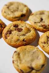 A detailed view of golden brown chocolate chip cookies arranged on a white surface, showing melty chips and soft texture under natural light. No visible branding