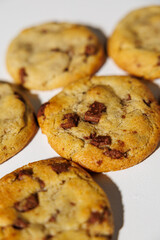 A detailed view of golden brown chocolate chip cookies arranged on a white surface, showing melty chips and soft texture under natural light. No visible branding