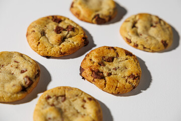 A golden brown chocolate chip cookie in sharp focus, highlighting its soft texture and melted chocolate bits, with others blurred in the background. No visible branding