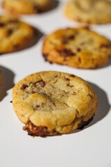 A golden brown chocolate chip cookie in sharp focus, highlighting its soft texture and melted chocolate bits, with others blurred in the background. No visible branding