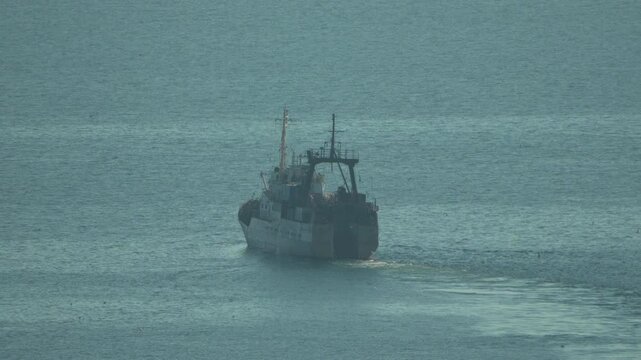 Ship ocean transport vessel moving away on calm sea water during the day.