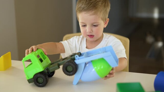 Toddler playing with toy truck and cement mixer while boy focuses on colorful block at table play in indoor room child explores toy and practices coordination with truck mixer block and learning