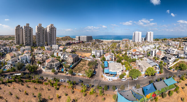 Aerial view of buildings and houses interspersed with greenery under a bright sky, offering a glimpse of the sea, Rishon LeZion, Center District, Israel.