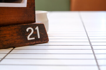 Wooden table number 21 placed on a white tile table in a cafe. Perfect for restaurant menu designs, reservation concepts, or minimalist cafe backgrounds.