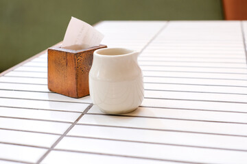White ceramic cup and wooden block placed on a white tile table in a cafe with natural light. Perfect for minimalist design concepts, restaurant branding, or lifestyle visuals