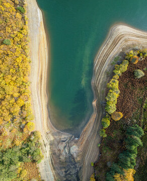 Aerial view of the vibrant autumnal shoreline meeting the serene, teal waters, a dance of earthy yellows and deep greens, Haddington, Scotland, United Kingdom.