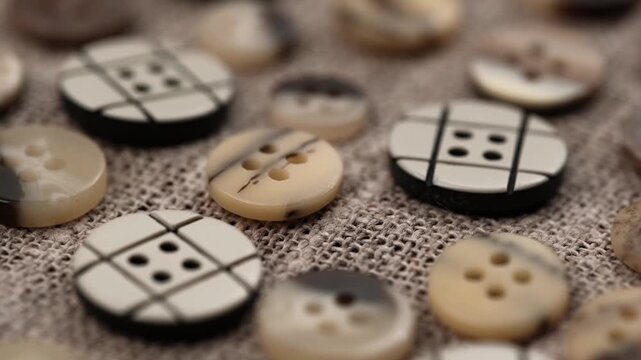rotation various decorative sewing buttons and tailoring accessories lying on rough linen fabric. collection includes vintage and modern styles, perfect for needlework, fashion, and crafts. close up.