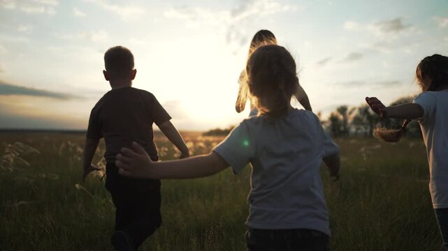 Child running through tall grass at sunset with friend across open field and meadow under wide sky showcasing nature and family play and running energy among grass silhouettes and gentle warm light