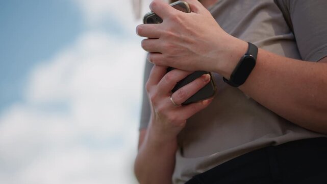 Close up of woman with bag strap holding phone outdoors and pressing it to chest under sunlight, subtle motion capturing emotional moment of hesitation