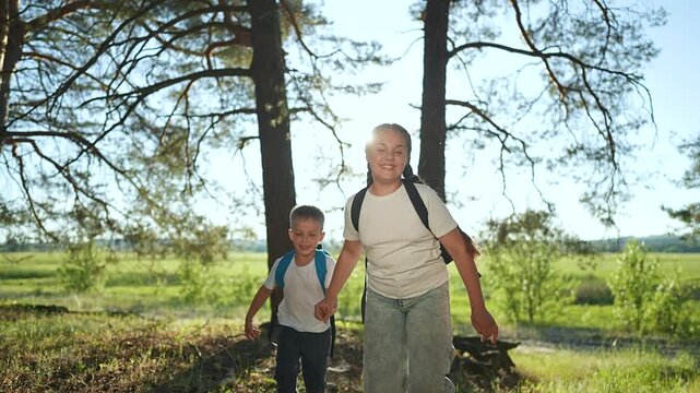 Boy blue backpack holds girl hand carefully walking forest path. Child steps close to sister under bright trees. Together boy girl explore nature. Forest gives child joy as girl guides boy outdoors.