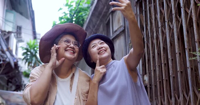 Happy senior asian women travelers taking selfie in narrow alley smiling friendship vacation exploring culture enjoying retirement lifestyle city travel journey happiness outdoor adventure