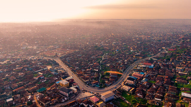 Aerial view of a sprawling urban landscape with densely packed buildings and a winding road cutting through the scene, bathed in the soft glow of the setting sun, Ibadan, Oyo, Nigeria.