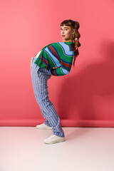 Stylish young woman in playful pose against vibrant pink background showcasing fashion creativity