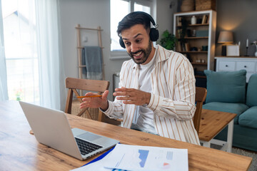 Young freelancer leading an online video meeting from a cozy home office smiling man with...