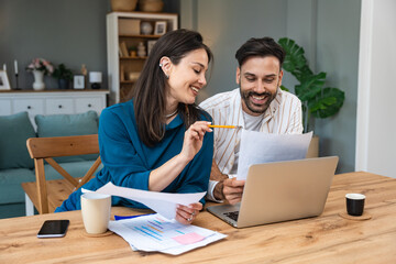 Fototapeta premium Smiling couple planning finances at home, reviewing charts, budgeting on laptop, discussing monthly expenses and savings goals together at the table during a positive teamwork session