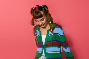 Stylish young woman with playful hairstyle posing against a vibrant pink background