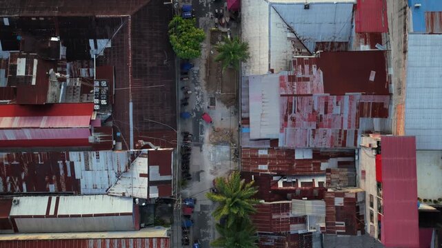 Aerial top down perspective showing rusty, corrugated metal roofs of impoverished district in Iquitos, Peru, with mototaxis moving
