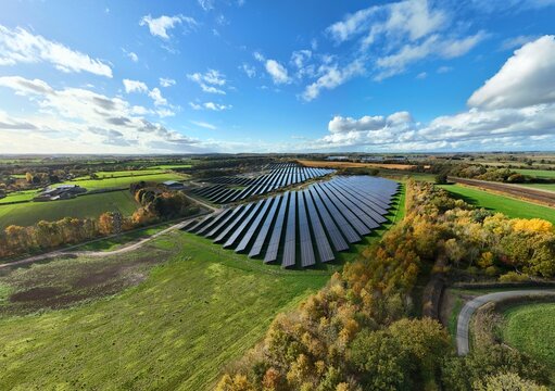 Aerial view of rows of solar panels reflecting the sky amidst green fields and autumn trees, Mansfield, England, United Kingdom.