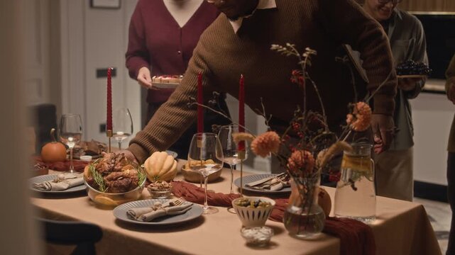 Tilt down shot of young bicultural couple serving table with homemade food while gathering with friends for Thanksgiving celebration