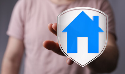 Hand holding a house symbol on a shield. Concept of real estate, security, and property protection....