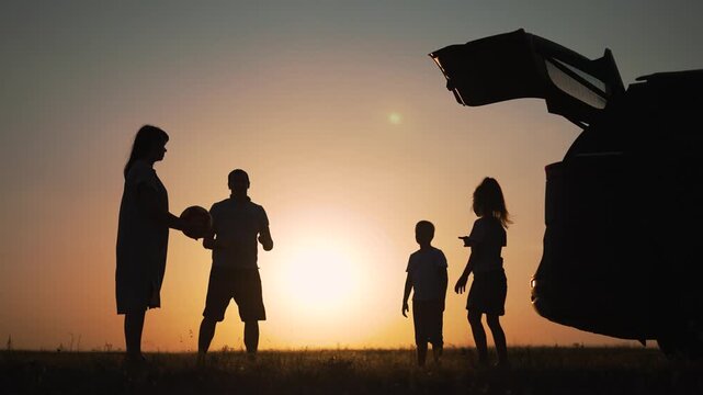 Family silhouette beside car trunk at sunset over field, mother father and child interact near car, travel pause showing connection and calm, silhouette and sunset highlight family bond roadside stop