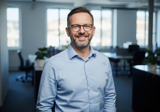 Smiling middleaged man glasses wearing a blue shirt in an office environment - Powered by Adobe