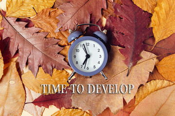 Vintage alarm clock on colorful autumn leaves with motivational text for seasonal inspiration