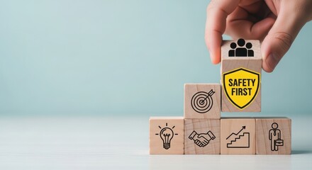 Hand stacking wooden blocks with safety first shield and business icons symbolizing growth and teamwork