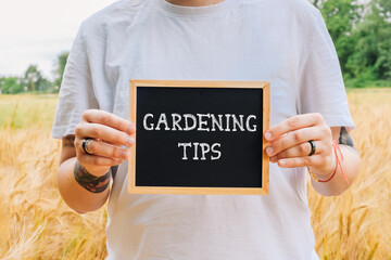 Individual holding a chalkboard sign displaying gardening tips in a golden field of wheat