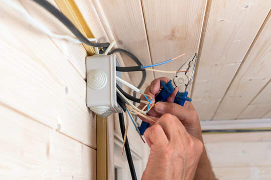 Electrician connects copper wires in a junction box on wooden wall, carefully twisting and securing cables during house wiring installation.