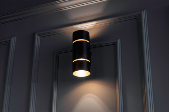 Modern black wall sconce emits soft light on a textured gray wall, creating a cozy, stylish ambiance with gentle upward and downward illumination.
