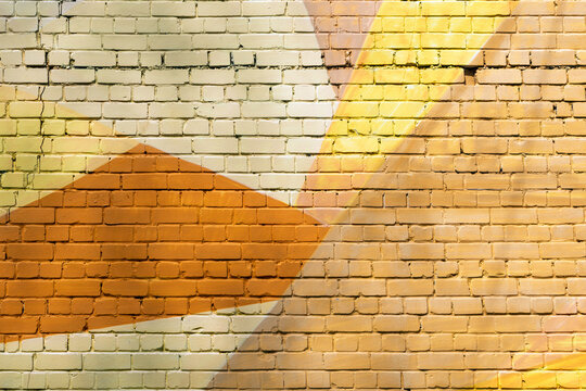 Sunlit brick wall with warm abstract mural shapes in orange and yellow tones, textured mortar lines form a vibrant urban background.