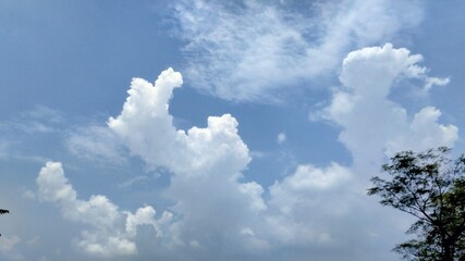 Fluffy white clouds drift across a clear blue sky on a bright summer day.