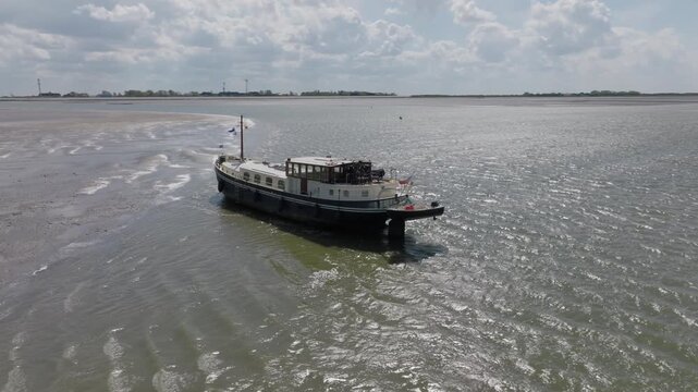 Traditional vessel grounded on shallow tidal flats at low tide; stern three‑quarter perspective in daylight.