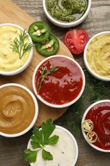 Different sauces and herbs on wooden table, flat lay
