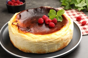Tasty Basque cheesecake with raspberries and mint on grey textured table, closeup