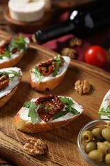 Delicious bruschettas with cream cheese, sun-dried tomatoes, arugula and bottle of wine on wooden table, closeup
