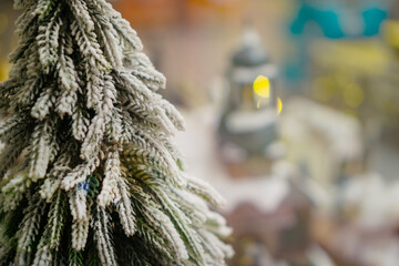 a snow covered miniature pine tree with bokeh lights and soft snowfall effect in a Christmas village concept of holiday advertising, winter celebration, festive greeting