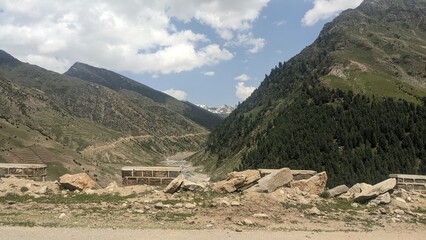 Majestic mountain pass with winding road and lush green slopes under a cloudy sky.