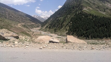 Majestic mountain valley with winding road and lush green slopes under a clear blue sky.