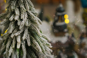 a snow covered miniature pine tree with bokeh lights and soft snowfall effect in a Christmas village concept of holiday advertising, winter celebration, festive greeting