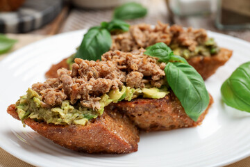 Delicious bruschettas with tuna, avocado and basil on plate, closeup