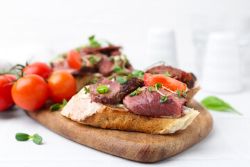 Delicious bruschettas with roast beef served on white table, closeup